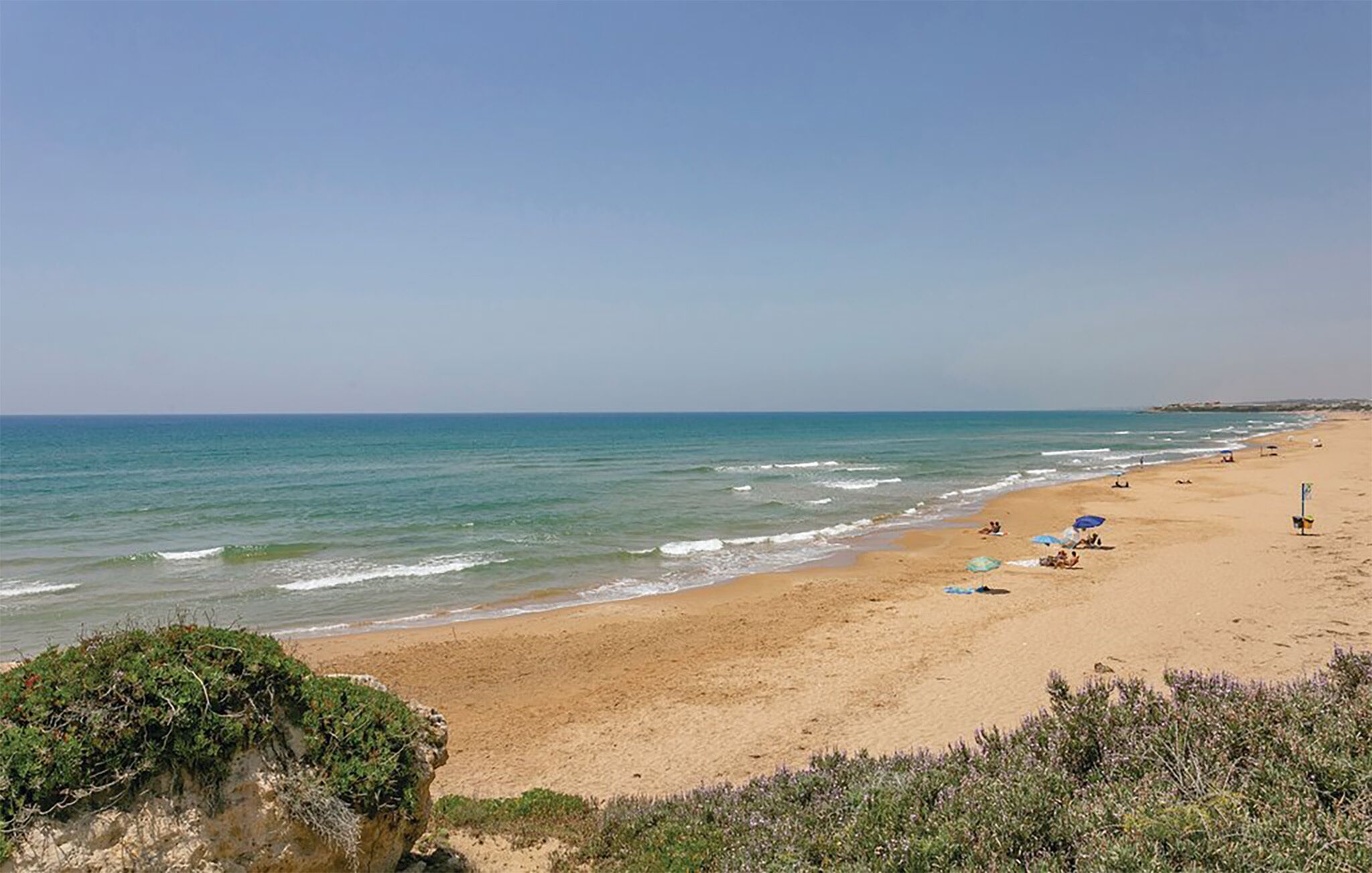 A beach with clear skies, calm waves, and a few people relaxing.