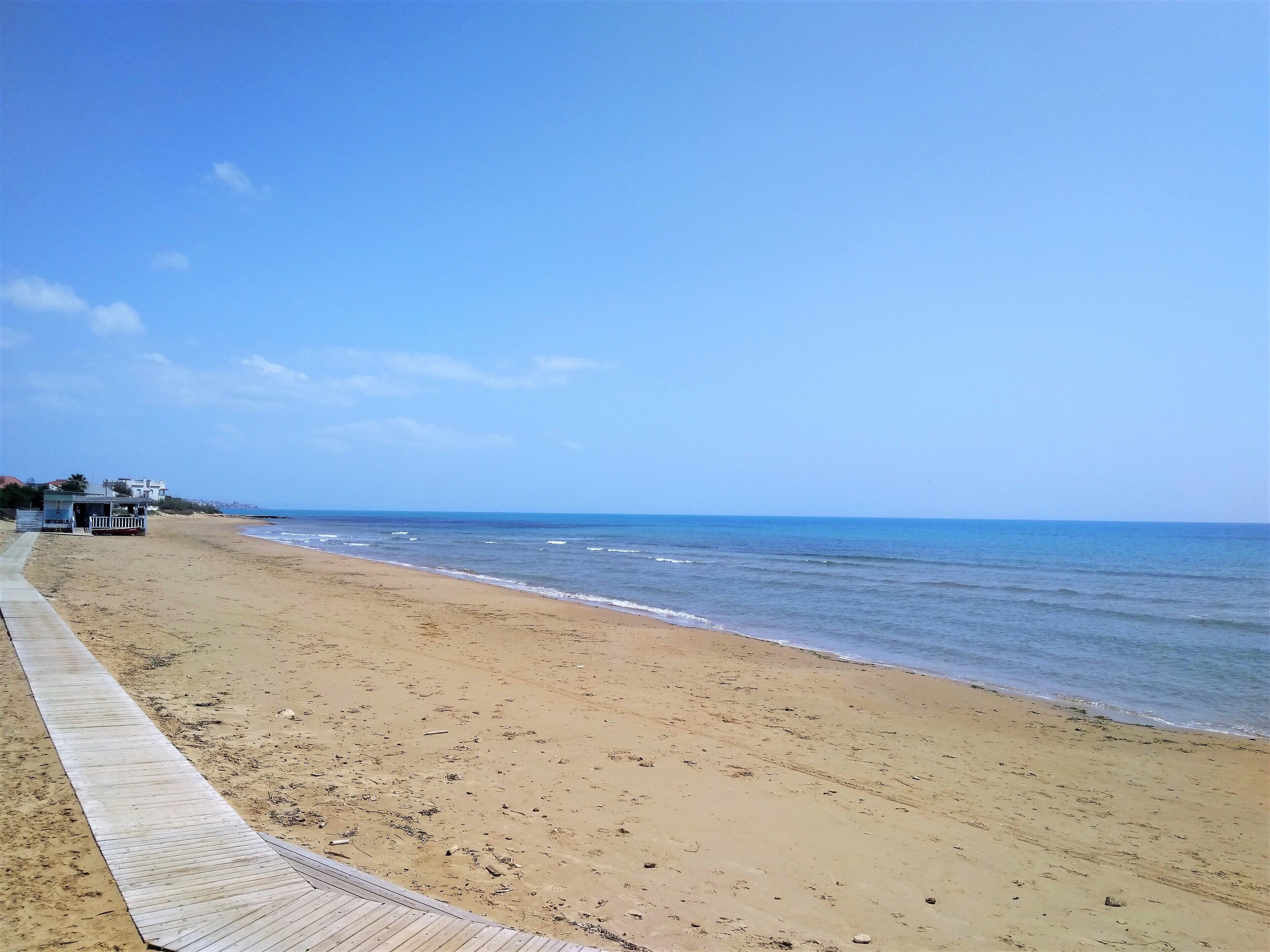A beach with a wooden walkway leading to a small structure, likely a beach hut or kiosk, and a clear view of the ocean.
