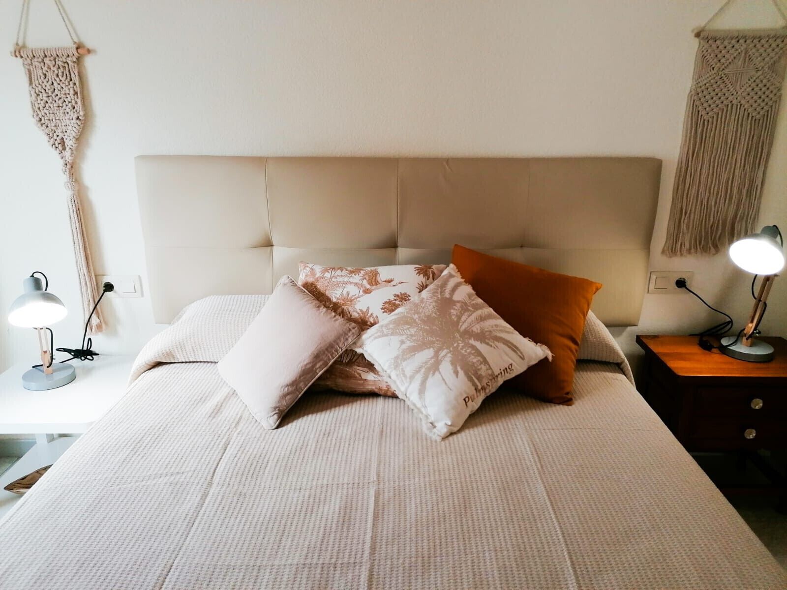 A neatly made bed with a white headboard, multiple pillows, and two bedside lamps on a nightstand.