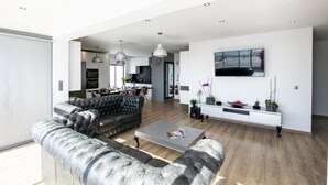 Un vaste espace de vie comprenant un canapé moderne, une table basse et un téléviseur à écran plat fixé au mur.