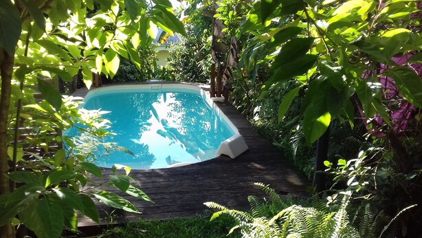 A swimming pool surrounded by lush greenery and a wooden deck. - Kay Zanndoli, sea view, pool, jacuzzi, garden (La Trinité)