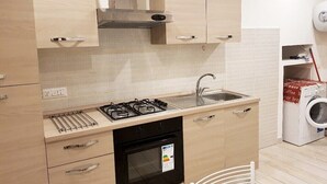 Een compacte keuken met een gasfornuis, spoelbak en een inbouwoven. Ook aanwezig is een wasmachine en een klein schap met spullen.