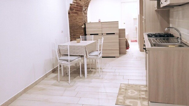 Een kleine keuken met een bakstenen boog, een eethoek met een tafel en stoelen, en een ingebouwde kookplaat.