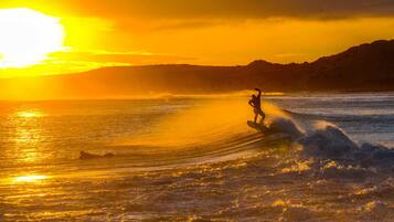 A surfer riding a wave at sunset with a mountainous backdrop.