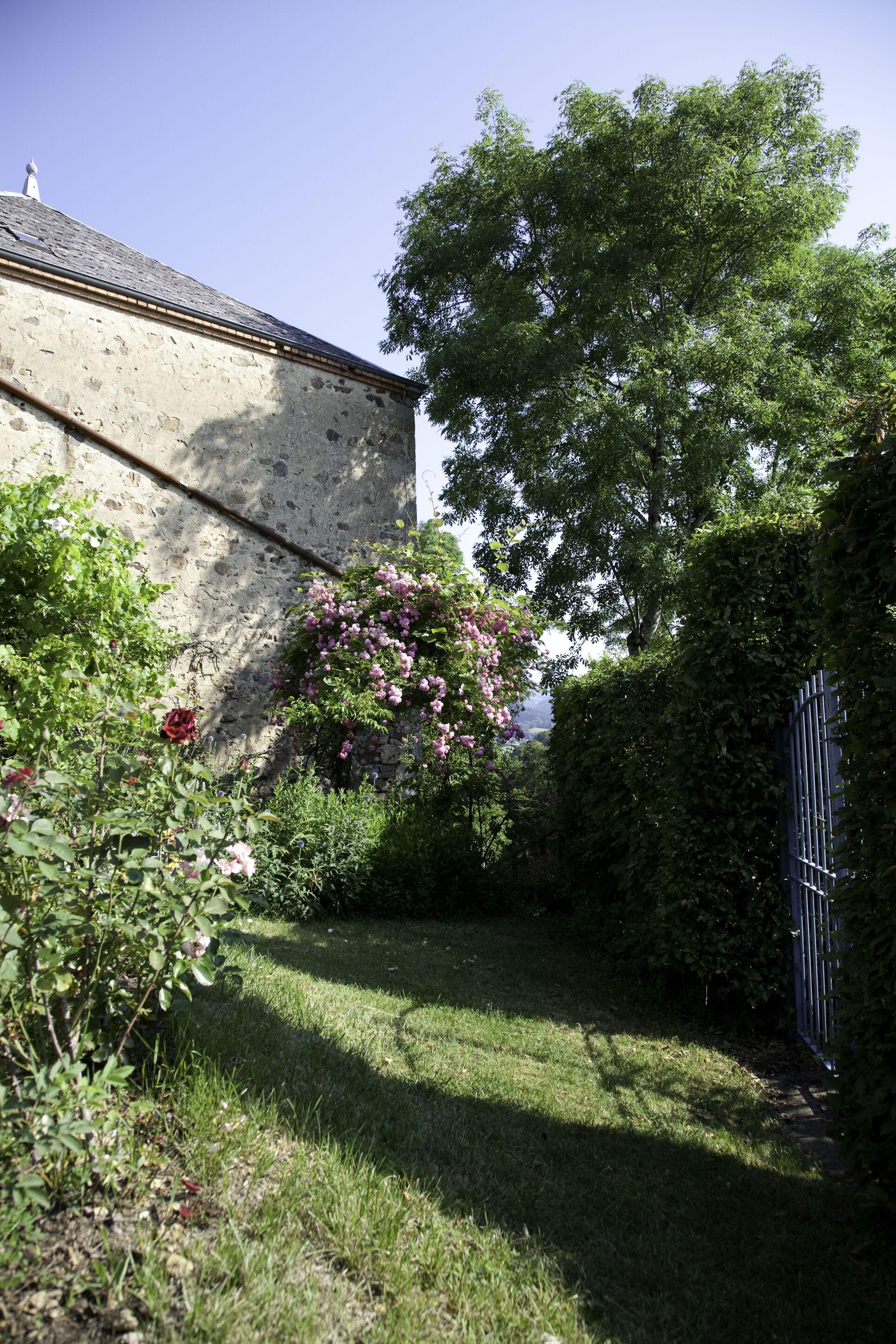 Ein Steinhaus mit einem grasbewachsen Garten, einem Metalltor und einem großen Baum.