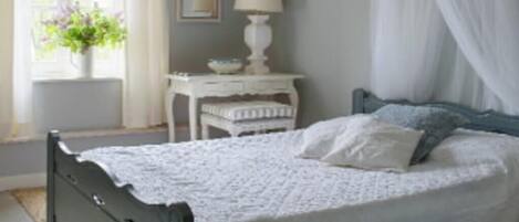 A bedroom with a bed, a bedside table with a lamp, a window with curtains, and a hanging light fixture.