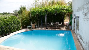 Une piscine rectangulaire dont les bords sont recouverts de carreaux, entourée d’une pelouse et d’un mur blanc.