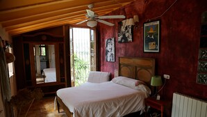 Une chambre avec un grand lit, un ventilateur de plafond et des œuvres d’art accrochées aux murs.