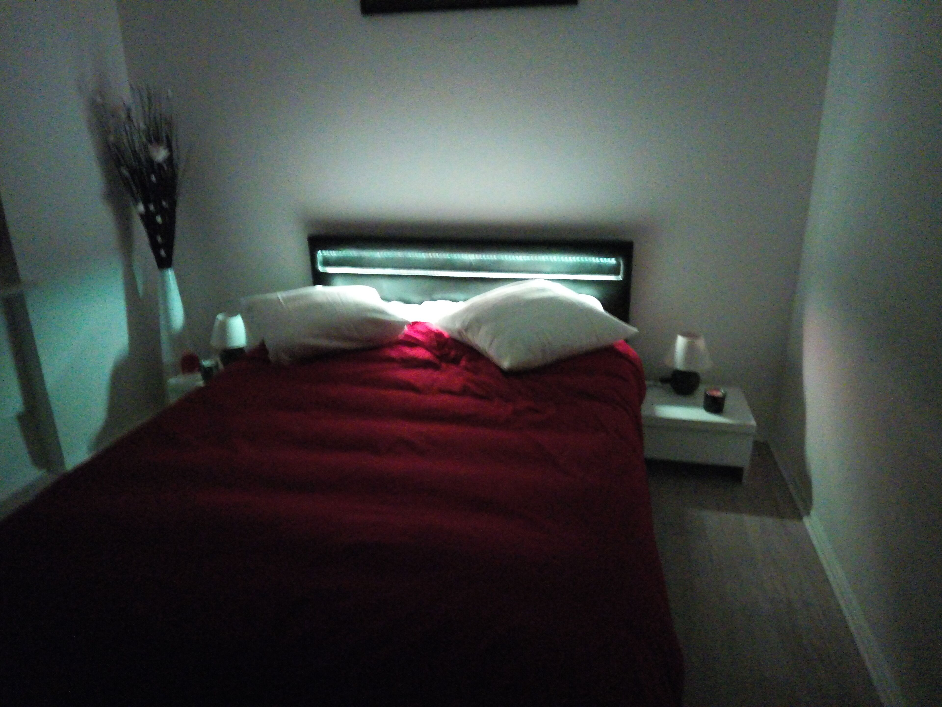 Una camera da letto con un letto, cuscini, un comodino e una lampada a parete.