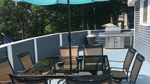 Eine Außenpatio mit Tisch, Stühlen, einem Grill und einem großen Sonnenschirm.