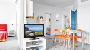 A modern living room with a flat-screen TV, a dining area with orange chairs, and a red sofa. - Le Capannelle - Figaro by Feeling Italy (Massa Lubrense)