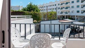 Une terrasse avec des chaises et une table en métal blanc, donnant sur un quartier résidentiel avec des immeubles et de la verdure.