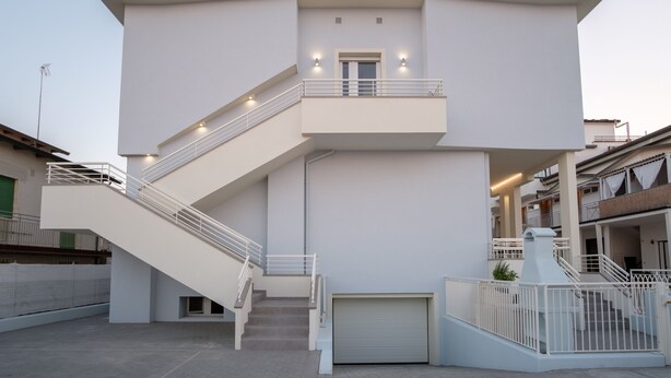 Un edificio moderno con una scala che conduce a un balcone, un portone garage e un cielo sereno.