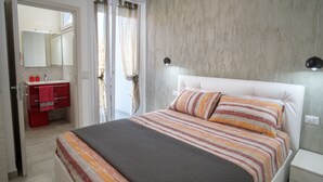 Una camera da letto con un letto, un comodino, un armadietto rosso e un bagno visibile attraverso una porta aperta.