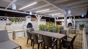 Una veranda esterna con tavolo e sedie in legno, un barbecue e piante in vaso.