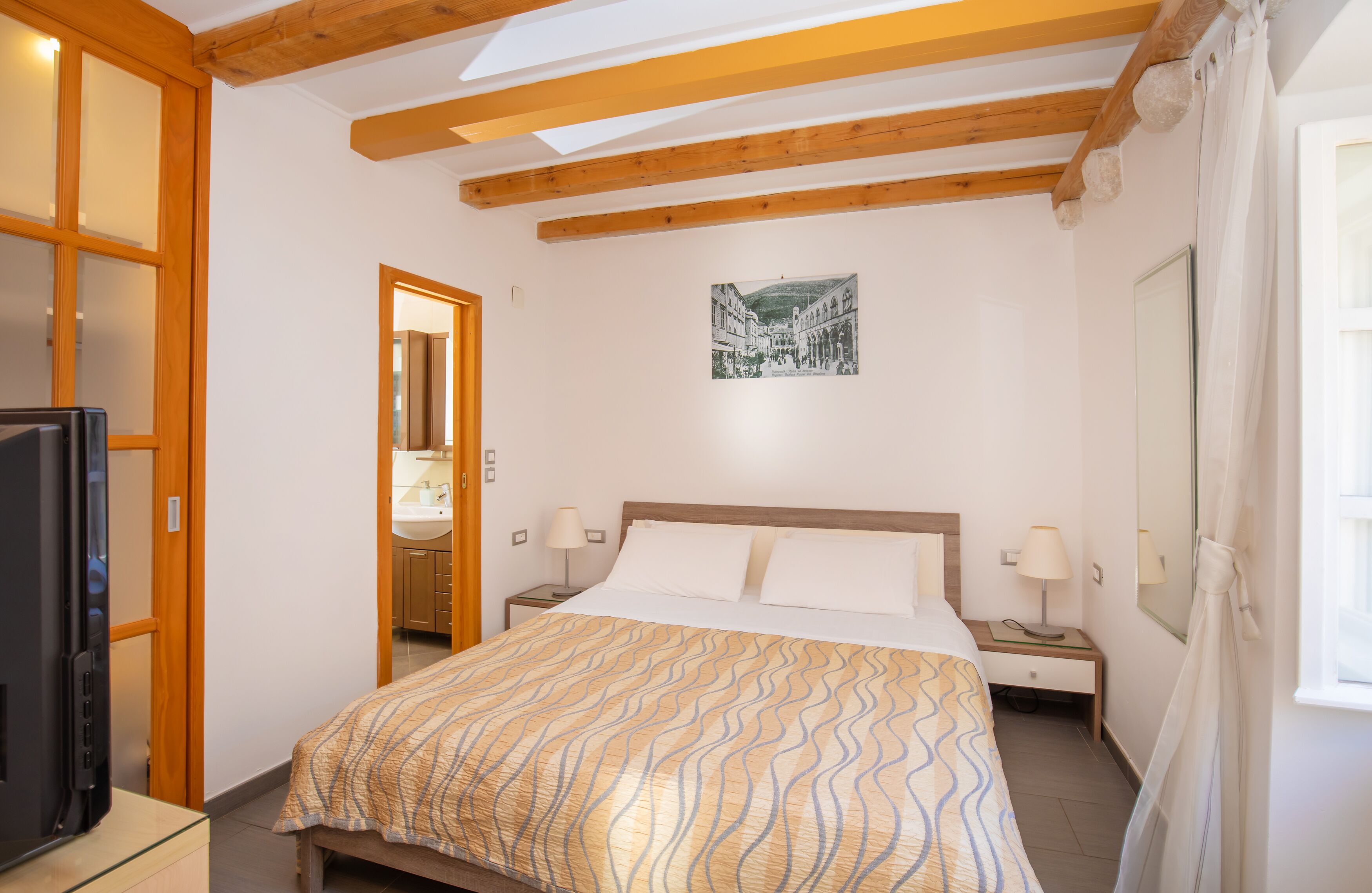 Une chambre à coucher avec un lit, des tables de chevet, une télévision et un tableau au mur.