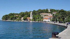 Une ville côtière avec une église imposante située sur une colline, une promenade en bord de mer et une mer d’un bleu limpide.