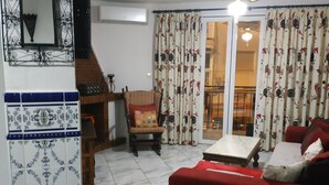 Ein Wohnzimmer mit einem roten Sofa, einer Holzkiste, einer gemusterten Wand und einem Deckenventilator.