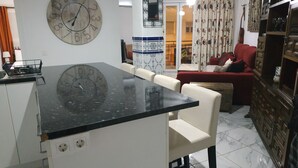 Eine Küche mit einer großen Kochinsel, weißen Stühlen, einem roten Sofa und einer dekorativen Wanduhr.