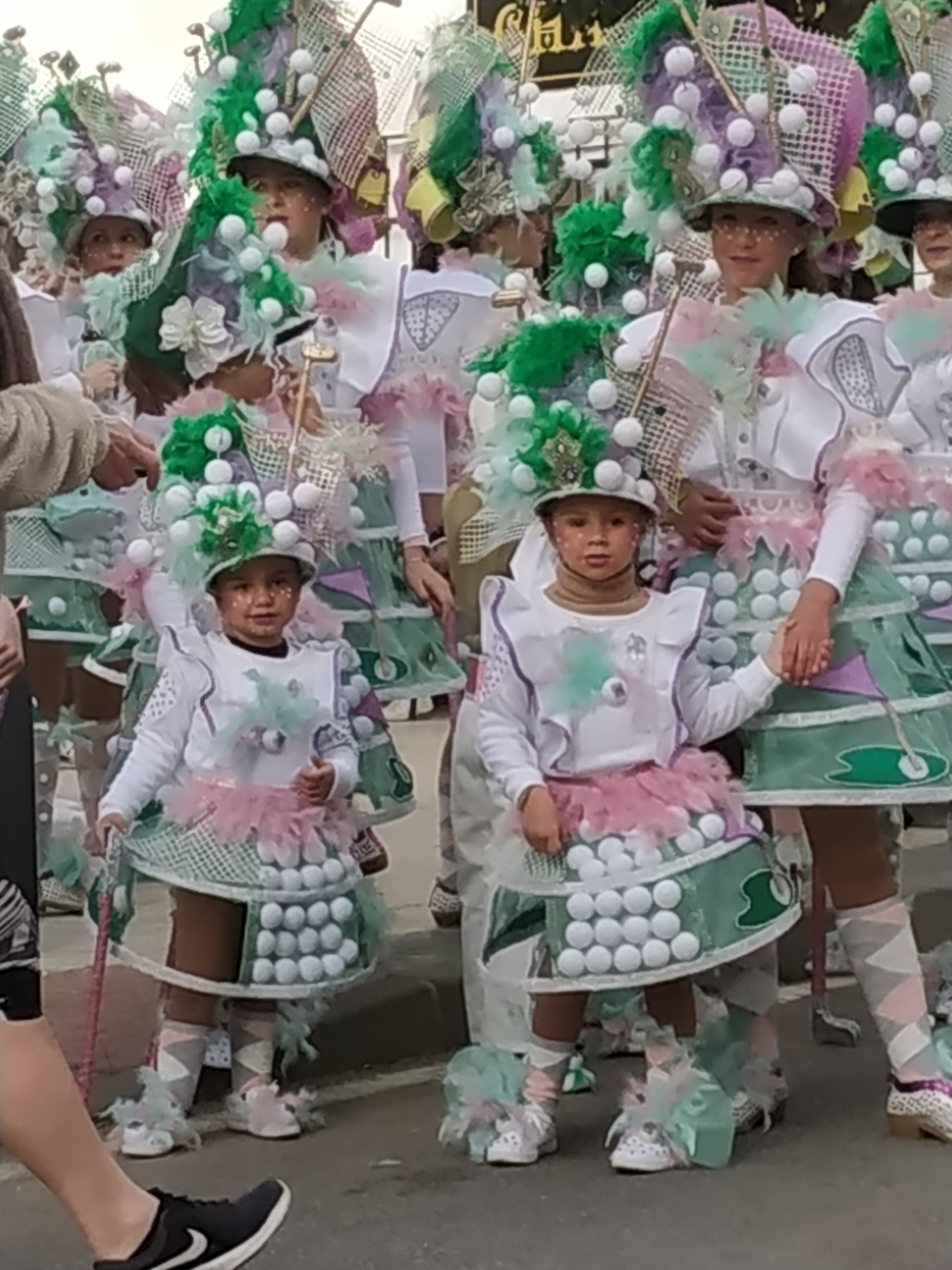 A group of children in colorful costumes with green, white, and pink elements, possibly for a parade or festival.