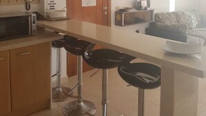 A kitchen with a microwave, a toaster, and a coffee maker on the counter. There are three bar stools in front of the counter.