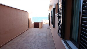 A narrow corridor with tiled flooring leading to a balcony with a view of the sea.