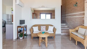 Una sala de estar con un sofá, una mesa redonda y un televisor. Se encuentra un área de cocina a la izquierda y una escalera a la derecha.