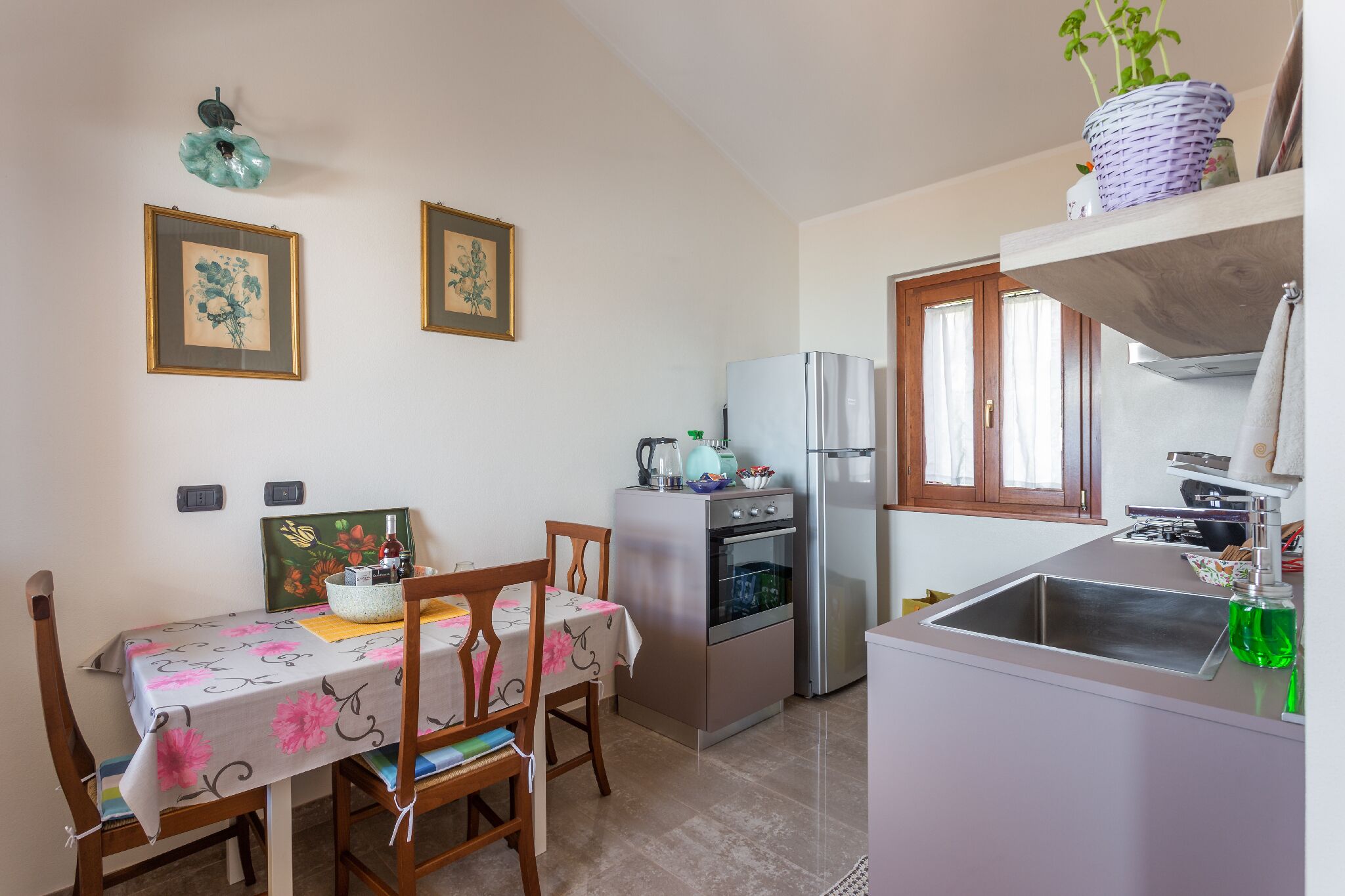 A compact kitchen with a refrigerator, oven, and sink. There is a dining table with chairs and a small window above the sink.
