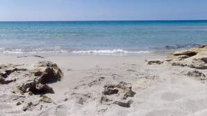 Una playa arenosa con aguas azules cristalinas y afloramientos rocosos.