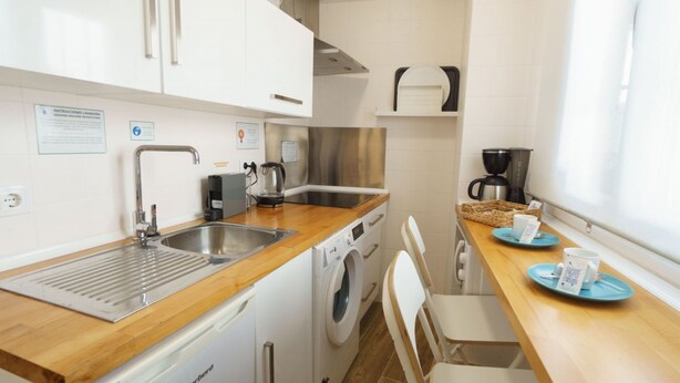 A compact kitchen with a stainless steel sink, a coffee maker, a washing machine, and a wooden countertop. - RentalSevilla Enladrillada Center City (Sevilla)