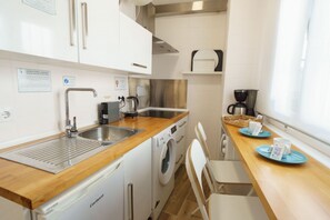 A compact kitchen with a stainless steel sink, a coffee maker, a washing machine, and a wooden countertop. - RentalSevilla Enladrillada Center City (Sevilla)
