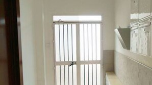 A narrow hallway with a white door featuring vertical bars, a small window, and a tiled wall with a built-in shelf. - RentalSevilla Enladrillada Center City (Sevilla)
