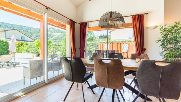 Een eetruimte met een grote tafel, stoelen en een hanglamp.
