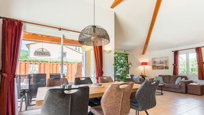 Een ruime woonkamer met een eettafel, stoelen, een bank en een groot raam.