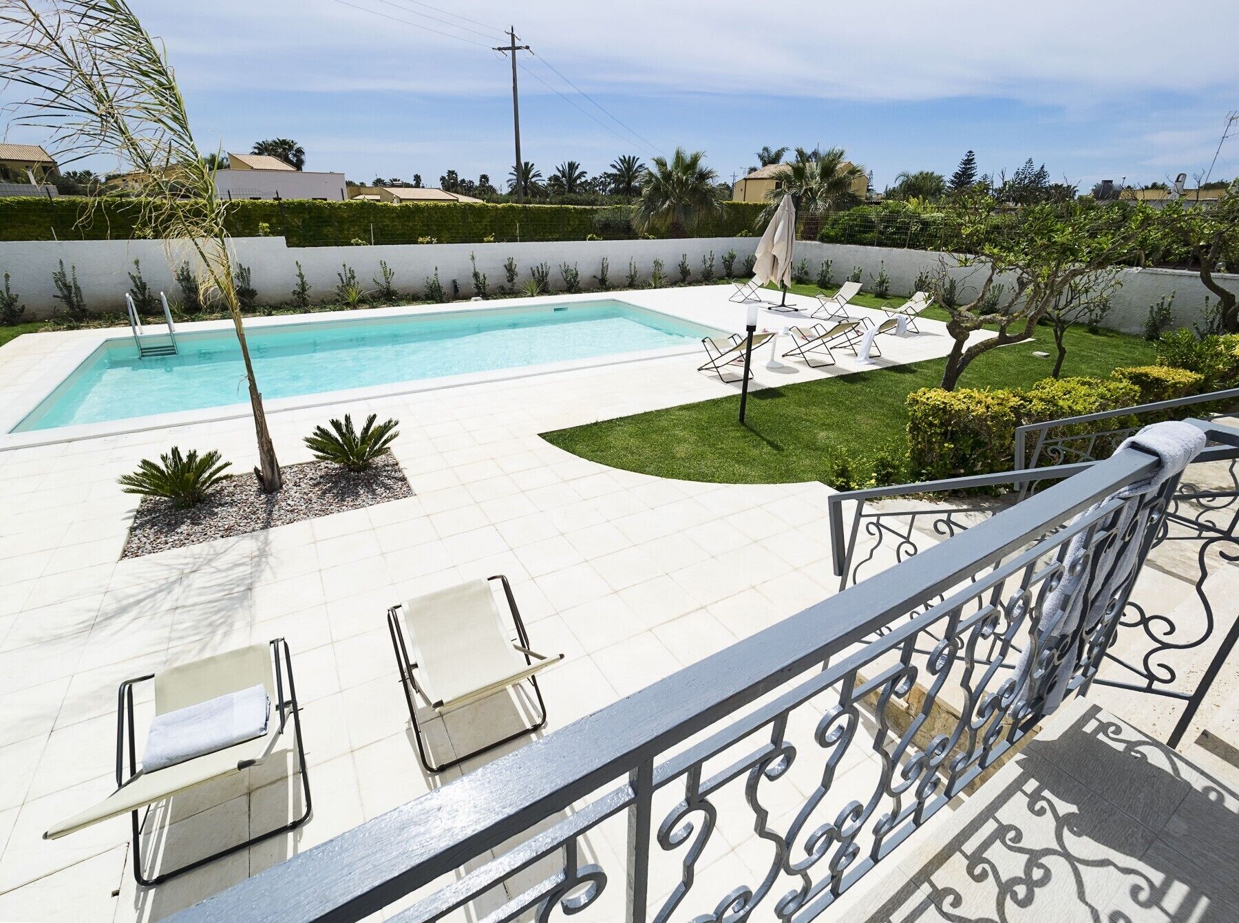 Une piscine avec des chaises longues et un petit espace aménagé en jardin.