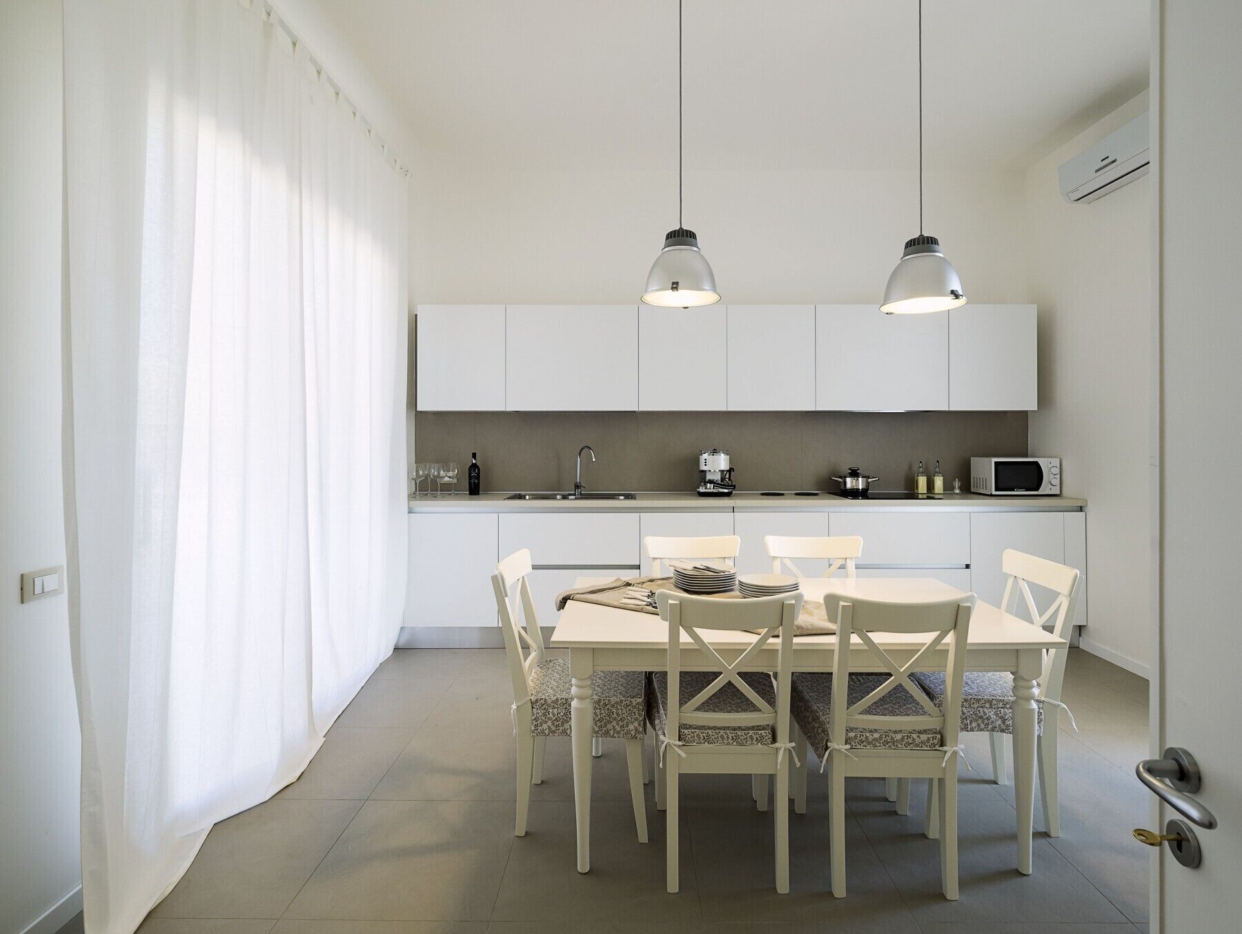 A modern kitchen with white cabinets, a dining table with chairs, and pendant lighting.