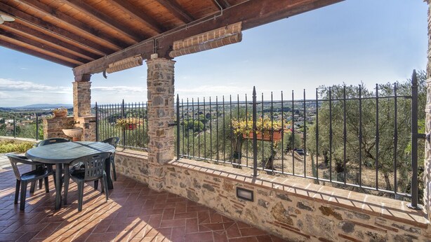 Eine überdachte Terrasse im Freien mit Steinsäulen, einem Tisch und Stühlen und Blick auf die Landschaft.