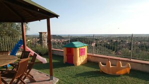 Eine Terrasse mit Tisch, Stühlen, einer Rutsche, einem Spielhaus und einer kleinen Spielgefährte.