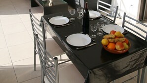 Ein Essbereich mit einem schwarzen Tisch, gedeckt für vier Personen, umgeben von Metallstühlen. Auf dem Tisch befinden sich eine Obstschale und eine Weinflasche.