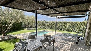 Ein überdachter Außenbereich mit Pool, Liegestühlen und einem Tisch.