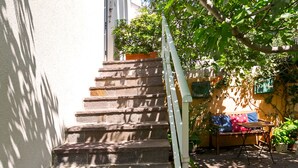 A stone staircase leading up to a building with a white exterior. There are potted plants and a small seating area with a table and chairs.