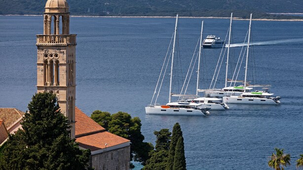 A coastal scene with a prominent tower and several sailboats anchored near the shore.