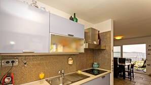 A modern kitchen with a large sink, a dining area with a table and chairs, and a view of the sea through a window.