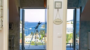 An open doorway leading to a balcony with a telescope, a "Closed" sign, and a view of the sea.