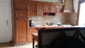 A kitchen with wooden cabinets, a tiled backsplash, a chandelier, and a black leather couch. - Very quiet family holiday home (Isigny-le-Buat)