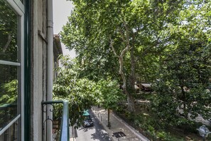 A street view with trees, a parked car, and a building with a green awning.