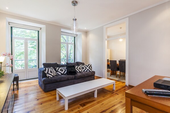 En moderne stue med en grå sofa, et hvidt sofabord og et spiseområde med stole og et bord.