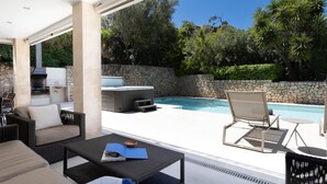 Eine Terrasse im Freien mit Pool, Sitzgelegenheiten und Grillplatz.