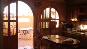 Une cuisine avec une table ronde et des chaises, une fenêtre donnant sur l’extérieur et une porte menant à un patio.