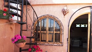 Un bâtiment doté d’un balcon en fer forgé, d’une grande fenêtre en arc de cercle et d’un pot de fleurs suspendu.